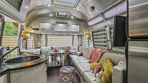 Interior compacto de una caravana con kitchenette, zona de comedor y sala de estar con cojines.