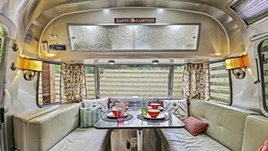 Un interior acogedor con una mesa preparada para dos, asientos cómodos y un letrero que dice "HAPPY CAMPERS".