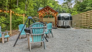 Un área de estar al aire libre con sillas Adirondack, un pabellón de madera y una zona de parrilla cubierta.