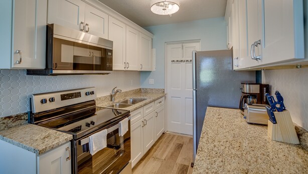 A kitchen with white cabinets, stainless steel appliances, a granite countertop, and a wooden floor. - Discover Micco charm, just a quick 23-min drive to Wabasso Beach Park (Micco)