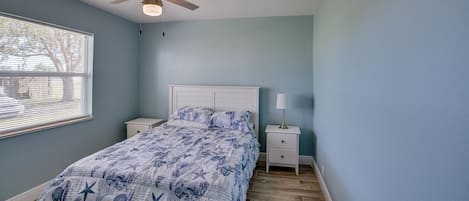 A bedroom with a bed, a ceiling fan, a nightstand, and a window with blinds.