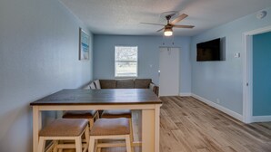 A dining area with a wooden table and four stools, a ceiling fan, a window with blinds, a flat-screen TV mounted on the wall, and a door. - Discover Micco charm, just a quick 23-min drive to Wabasso Beach Park (Micco)