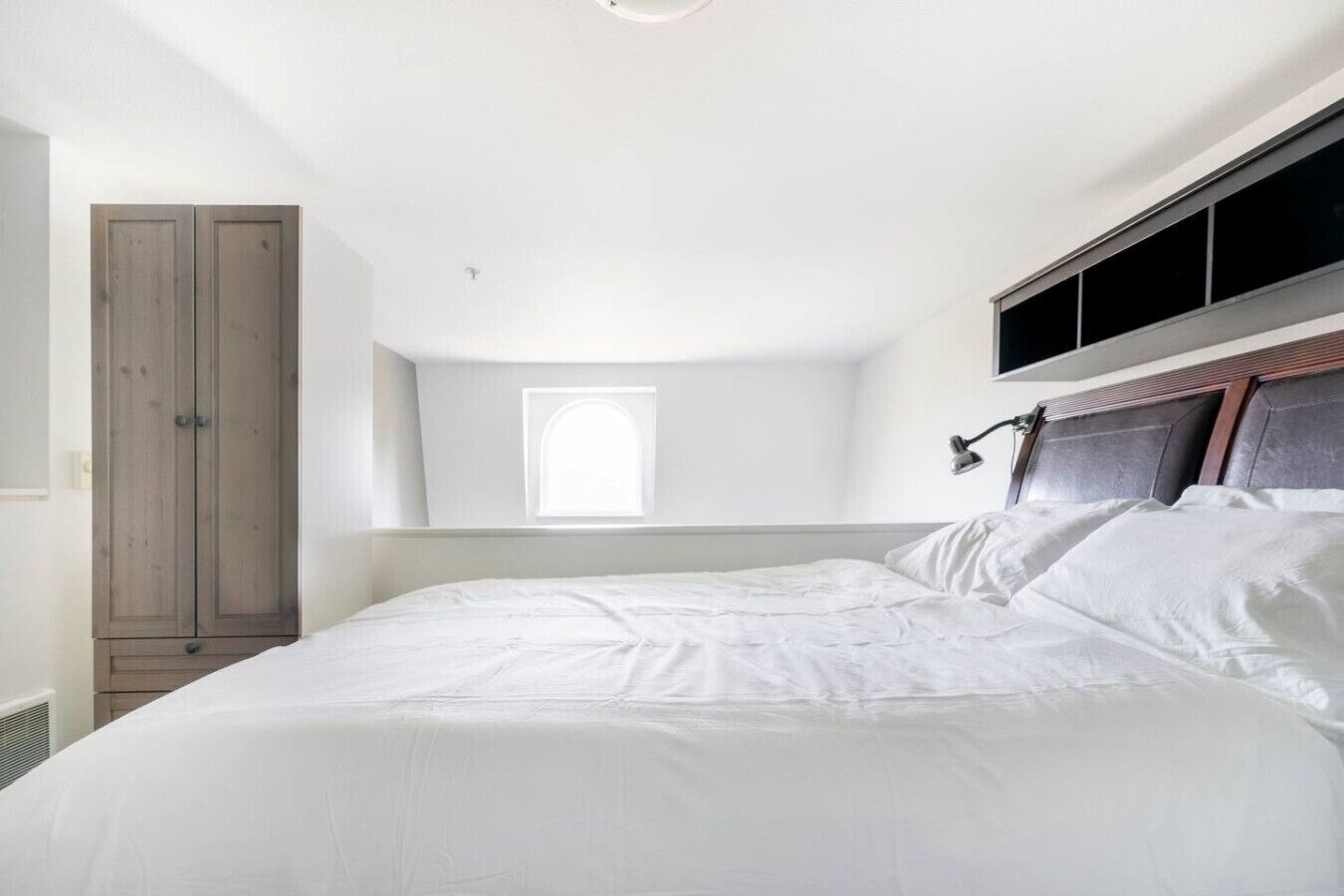 A bedroom with a large bed, a wardrobe, a window, and a ceiling light.