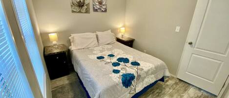 Une chambre à coucher avec un lit, deux tables de chevet, une porte et une fenêtre avec des stores.
