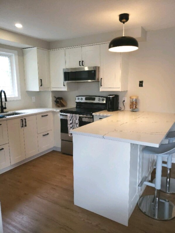 Enjoy cooking in this kitchen with a central island and bar stools, stainless steel range hood, and microwave.