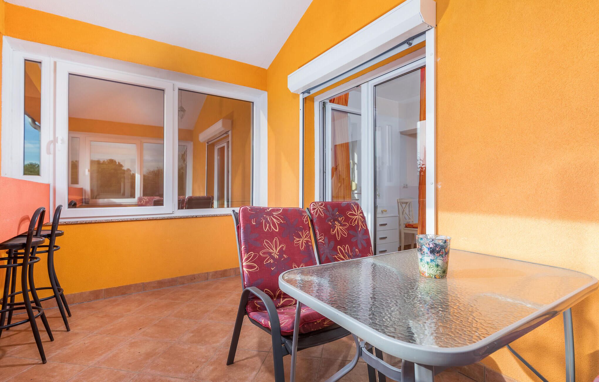 Un petit espace patio avec une table en verre et deux chaises, une fenêtre et une porte.