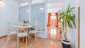 A dining area with a round table and chairs, a potted plant, and a sliding glass door leading to another room.