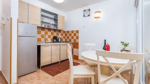 A compact kitchen with a refrigerator, a coffee maker, and a stove. There is a dining table with chairs and a small potted plant.