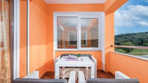Un balcone con un tavolo bianco e due sedie, una finestra e vista su un paesaggio verde.