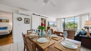 Un comedor con una mesa de madera dispuesta para cuatro, un ventilador de techo y vistas al exterior.