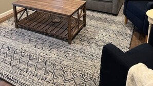 A living room with a gray sofa, a wooden coffee table, and a patterned rug. There are two windows with white frames and a view of greenery outside. - Beautiful Cabin in Red Lick Valley (Irvine)