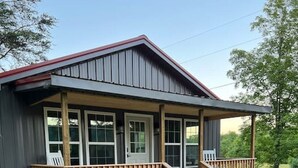 A single-story building with a covered porch, wooden railings, and a set of stairs leading to a door. - Beautiful Cabin in Red Lick Valley (Irvine)