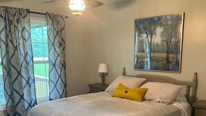 A bedroom with a bed, a ceiling fan, a nightstand, a lamp, and a painting on the wall. - Beautiful Cabin in Red Lick Valley (Irvine)