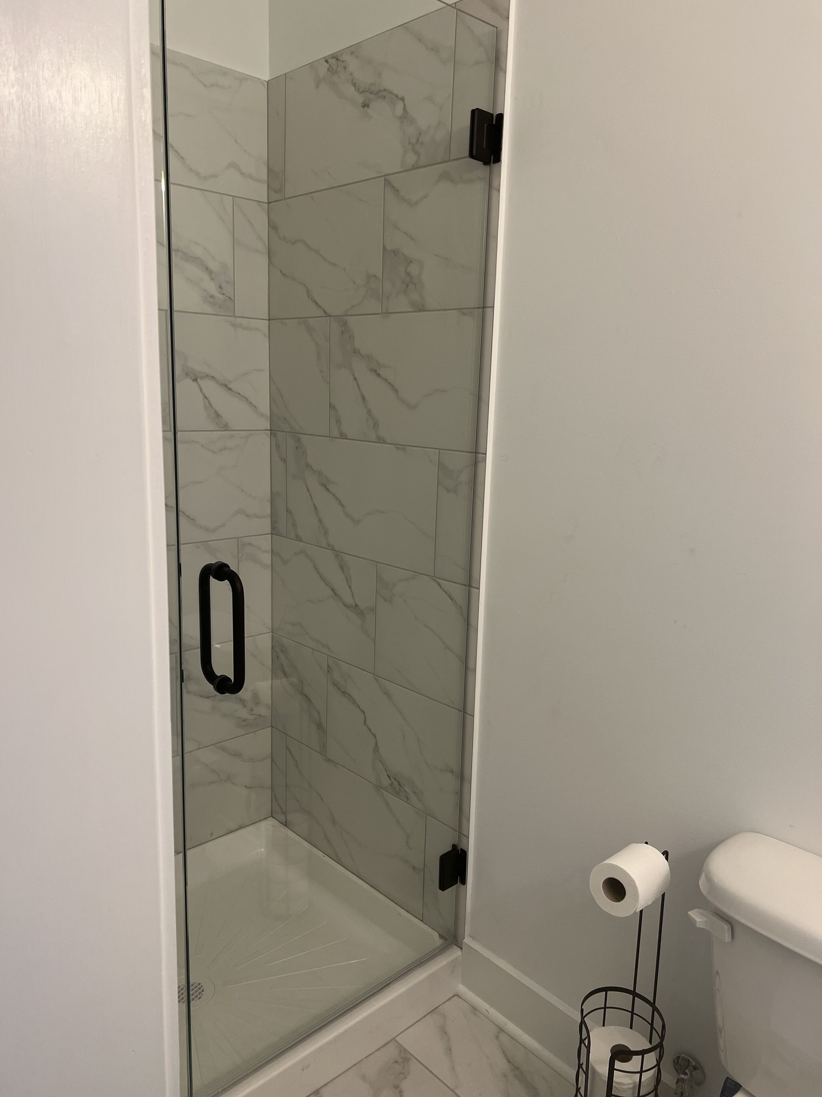 Une salle de bain avec une douche à parois de verre, des carreaux de marbre, des toilettes et un porte-rouleau de papier toilette.
