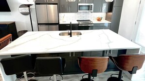 Een moderne keuken met een centraal eiland, roestvrijstalen apparatuur en hangende lampen.