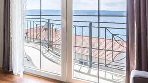 Une pièce dotée de grandes fenêtres donnant sur un balcon surmonté d’un toit recouvert de tuiles rouges et offrant une vue sur la mer.