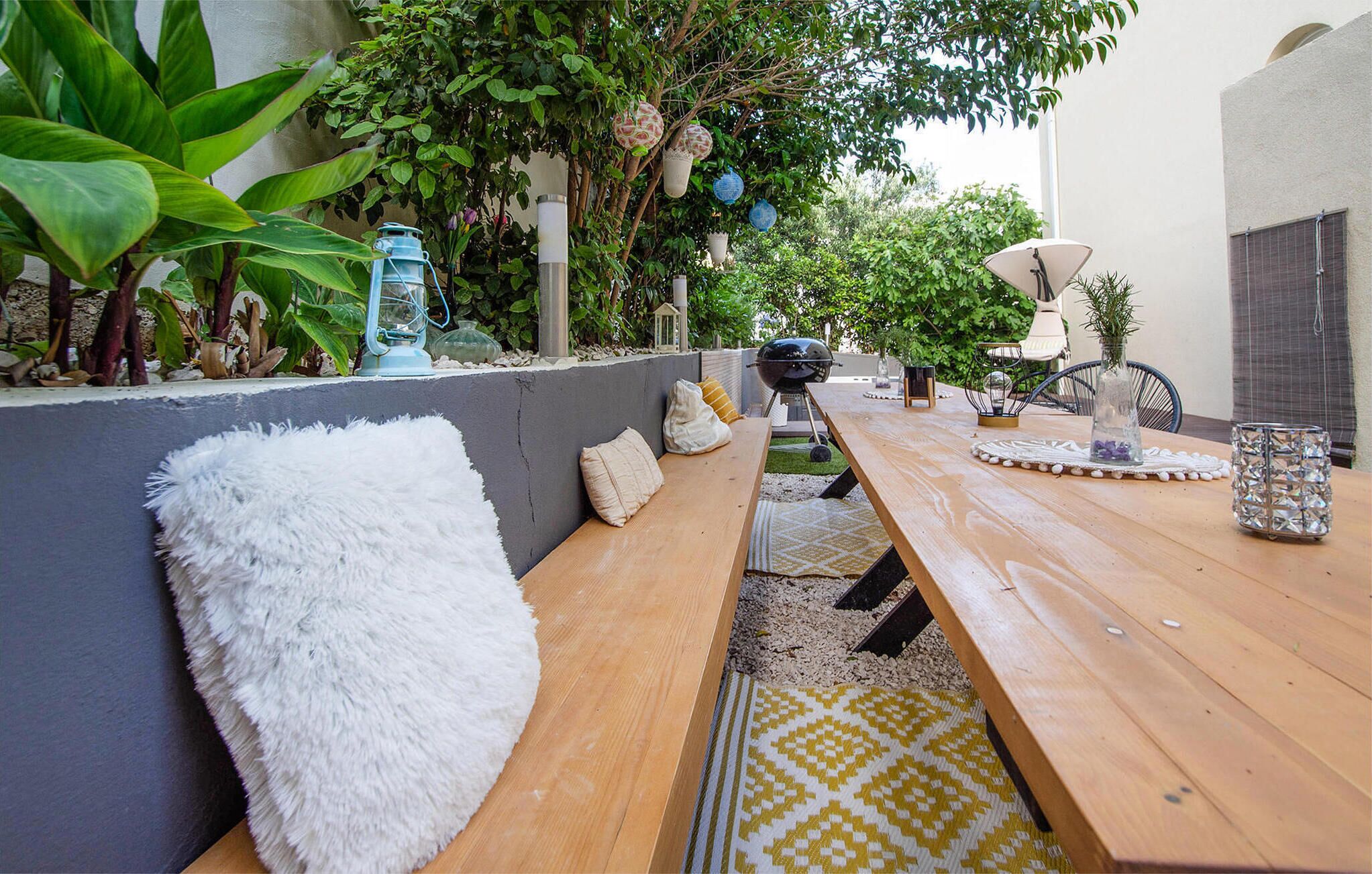 Een terras buiten met een houten tafel, bankjes en een barbecue.