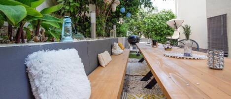 An outdoor patio with a wooden table, benches, and a grill.