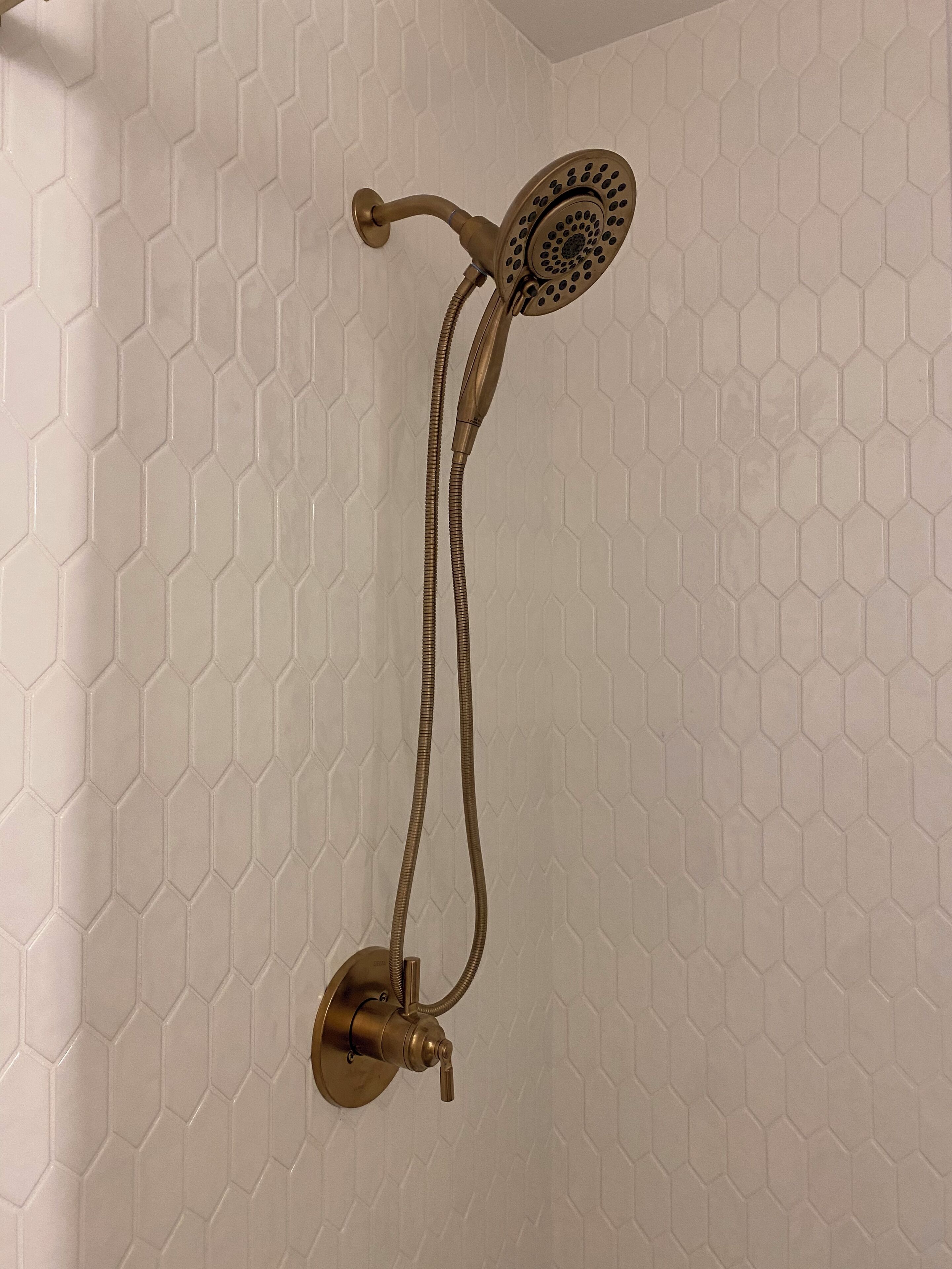 Un cabezal de ducha de latón con una manguera flexible conectada a una palanca fijada a la pared.