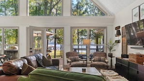 A spacious living area with a large window overlooking a deck, furnished with leather sofas, patterned armchairs, and a coffee table. - Private Lakefront Spread: BigH2O, Smokehouse, Spa, Firepits, Fence, PETS (Eatonton)