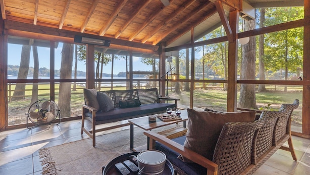 A wooden interior with a large window, a sofa, and a fan. - Private Lakefront Spread: BigH2O, Smokehouse, Spa, Firepits, Fence, PETS (Eatonton)