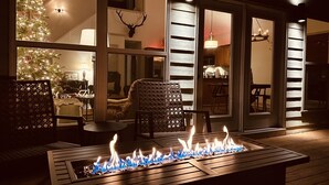 A cozy outdoor seating area with a fire feature, a Christmas tree, and a large window overlooking the interior. - Private Lakefront Spread: BigH2O, Smokehouse, Spa, Firepits, Fence, PETS (Eatonton)