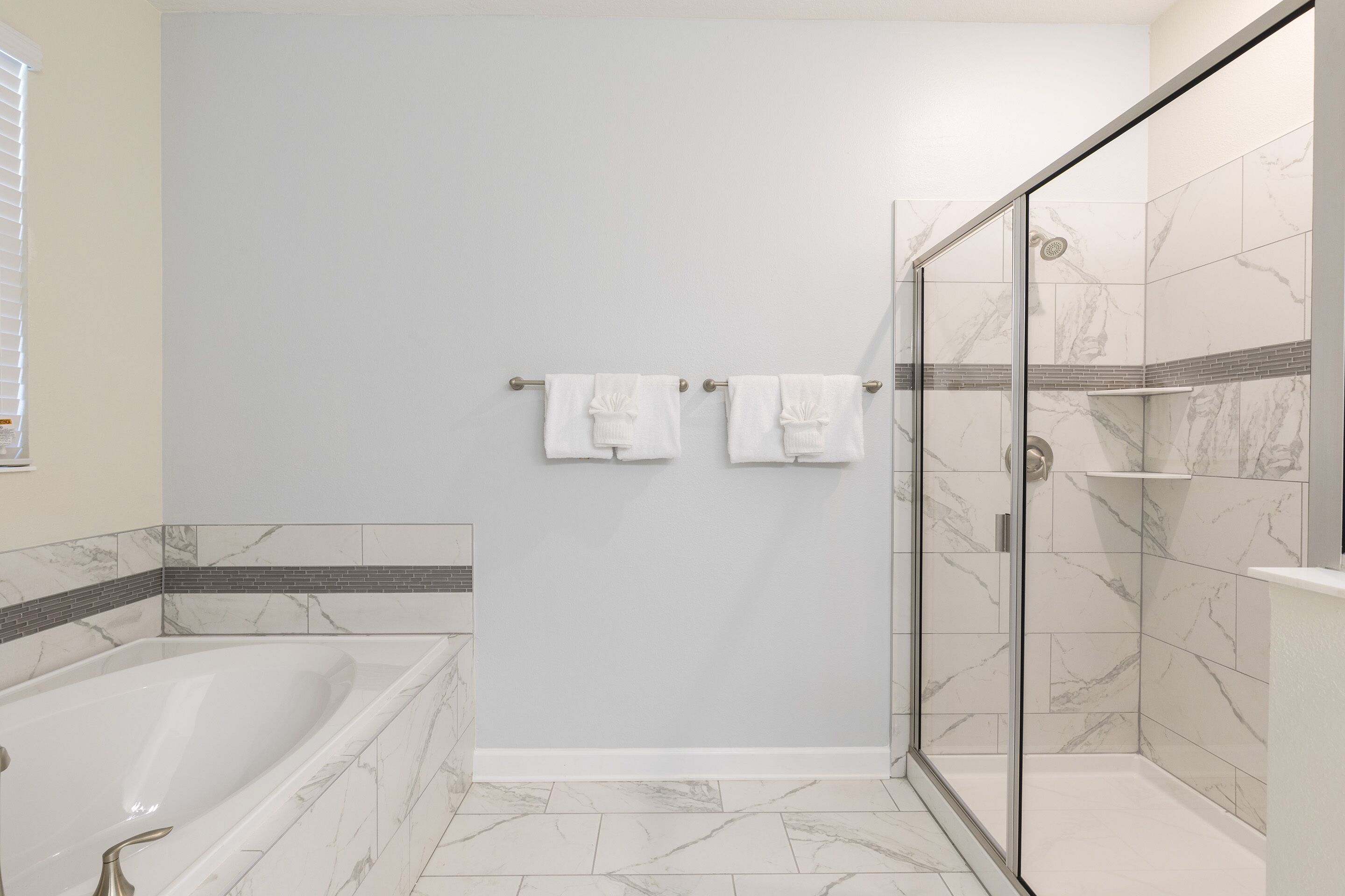 A modern bathroom with a glass-enclosed shower, a bathtub, and marble flooring.