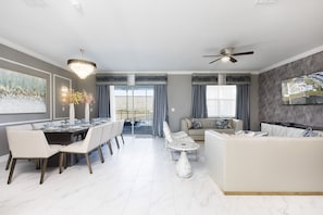 A modern living room with a dining area, a sofa, a TV mounted on the wall, and a ceiling fan. - Lakeview Luxury Villa in Storey Lake (Kissimmee)