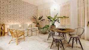 A modern living room with a stone wall, a sofa, a coffee table, and a dining area with chairs and a wooden table. - Gorgeous Republican. Apt inside old city. (cartagena)