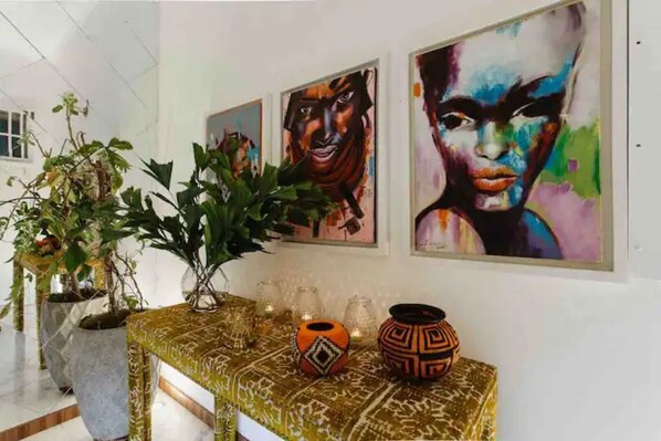 A hallway with a decorative table, potted plants, and three framed artworks on the wall.