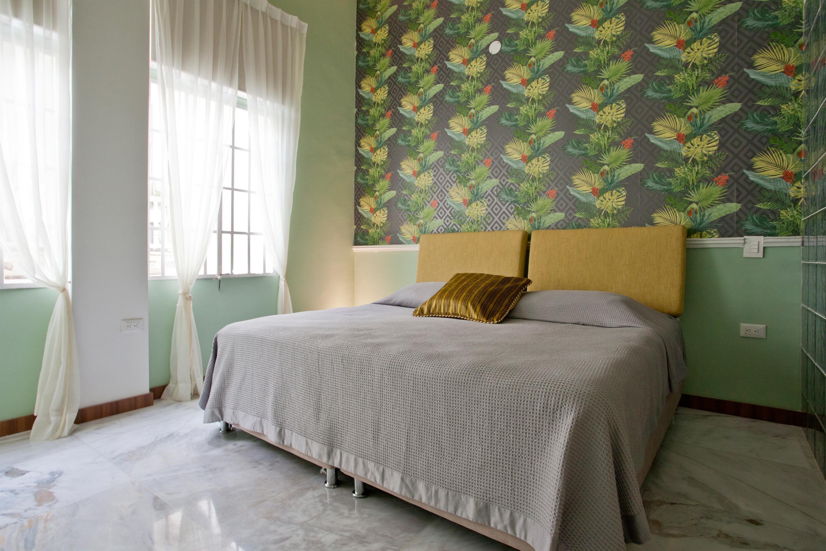A bedroom with a bed, a window with curtains, and a patterned wallpaper.