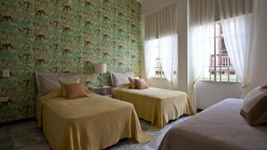 Ett hotellrum med två sängar, en mönstrad tapet och ett fönster med gardiner.