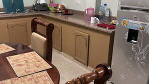 Een keuken met een eettafel, stoelen, een koelkast en een raam.