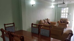 Een eetgedeelte met een houten tafel en stoelen, een bank en een raam met tralies.