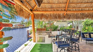 Un patio exterior con techo de paja, una parrilla y vista al agua.