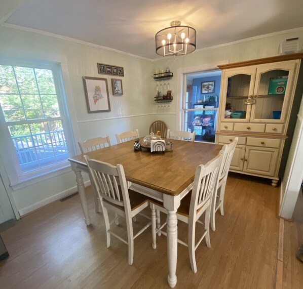 A dining area with a wooden table and white chairs, a chandelier, and a view through a window.