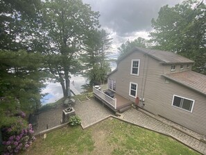 A two-story house with a patio, a small deck, and a view of a body of water.