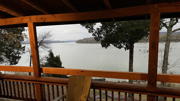 A wooden deck with a wooden chair, overlooking a calm lake with trees and hills in the background. - Derby Time Riverside Cabin (Derby)