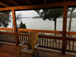 A wooden deck with a wooden chair, overlooking a calm lake with trees and hills in the background. - Derby Time Riverside Cabin (Derby)