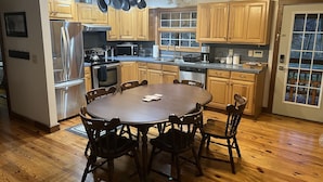 A modern kitchen with wooden cabinets, stainless steel appliances, and a dining area with a round table and chairs. - Derby Time Riverside Cabin (Derby)
