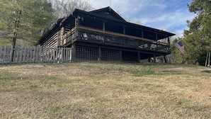 A two-story wooden cabin with a balcony, surrounded by a wooden fence and trees. - Derby Time Riverside Cabin (Derby)