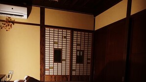 Ein traditioneller japanischer Raum mit Tatami-Böden, einem niedrigen Holzbett, einem Shoji-Bildschirm und einem Deckenventilator.