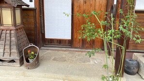 Eine traditionelle Holztür mit einem weißen Stoffvorhang, einer kleinen Laterne und einem Blumentopf davor.