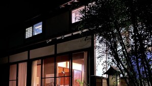 Ein traditionelles japanisches Gebäude mit großen Schiebegläsern, einem gepflasterten Innenhof und einer kleinen Holzhütte im Hintergrund.