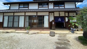 Ein traditionelles japanisches Gebäude mit einem Ziegeldach, großen Fenstern und einem Kiesweg zum Eingang.