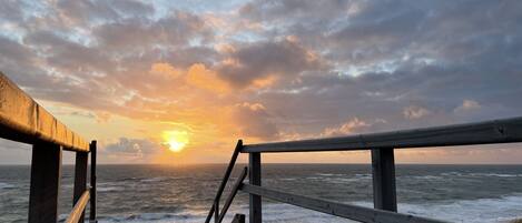 En träpromenad som leder till en strand med utsikt över havet och en solnedgång.