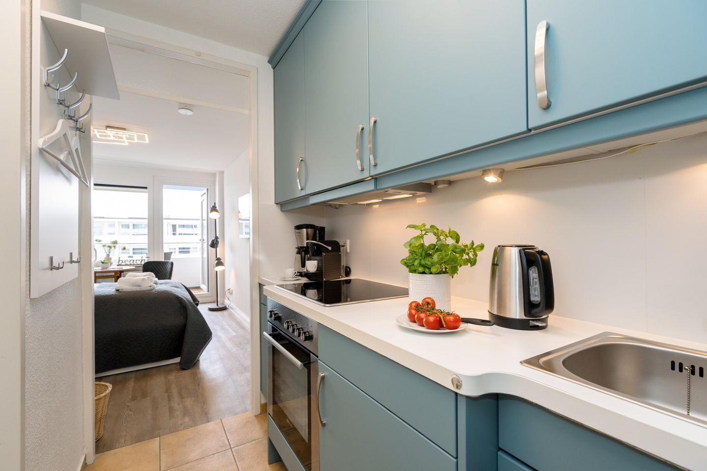 A modern kitchen with light blue cabinets, a coffee machine, a kettle, and a potted plant.