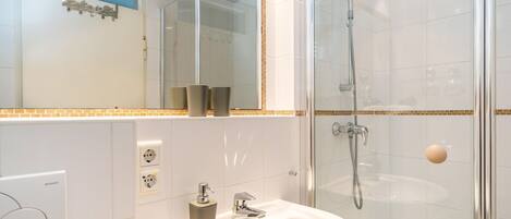 A modern bathroom with a glass-enclosed shower, a white sink, and a mirror with a decorative frame.