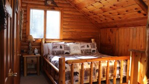 A wooden cabin bedroom with a bed, a nightstand, a window, and a door. - Seney Cabin with hot tub (Germfask)