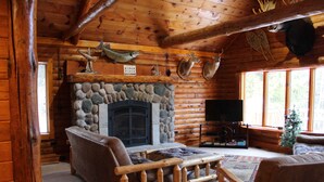 A log cabin interior with a stone fireplace, wooden furniture, and mounted animal heads. - Seney Cabin with hot tub (Germfask)